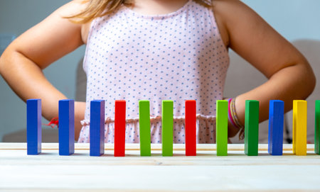 Wooden blocks arranged in a line, in the background a satisfied little girl. Concept of resilience, resistance, overcoming, failure, successの写真素材