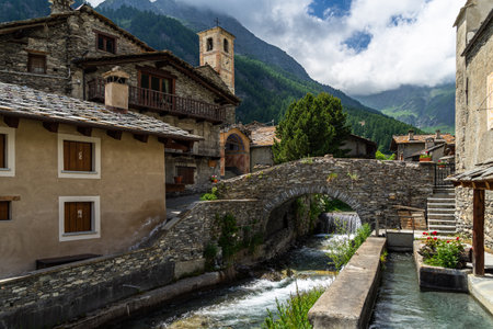 The charming village of Chianale in the heart of the Alps, with a picturesque river passing under stone bridge, Italyの写真素材