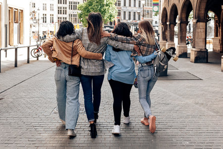 Back view of four friends hugging and walking in city center. urban lifestyleの写真素材