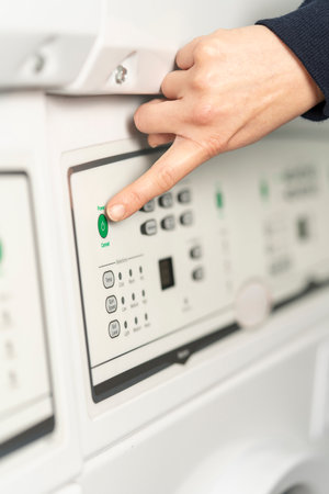 Close-up view of a hand about to press the green start button of the washing machine. Unrecognizable...