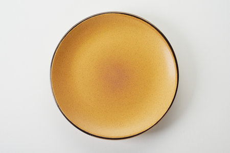 Top view of empty clean round yellow ceramic flat plate with black rim on white background