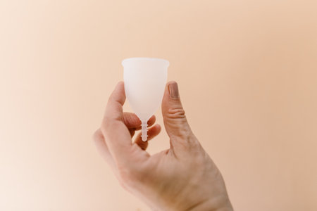 hand holding a menstrual cup in front of a peach backgroundの写真素材