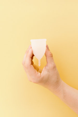 hand holding a menstrual cup with yellow backgroundの写真素材