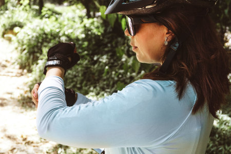 young Latin American woman with helmet and glasses adjusting the sleeves of her sports shirt. mountain bike concept.の写真素材