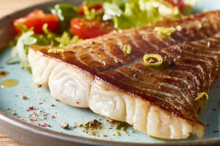 Closeup of tasty fish fillet and fresh vegetable salad served on plate in cafe