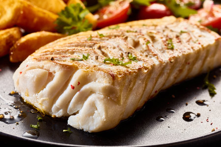 Closeup of palatable fillet of fish with herbs served on plate with rustic potato and vegetables in restaurantの写真素材