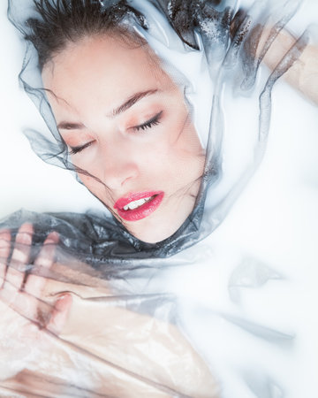 sensual woman creative portrait with black tulle in milk bathの写真素材