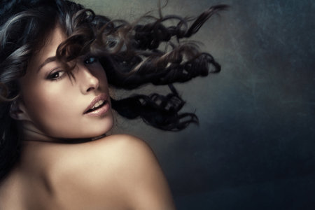 beautiful exotic tanned woman with long wavy hair in motion studio shot darker tonesの写真素材
