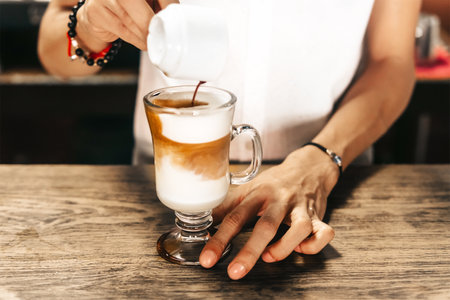 Unrecognizable hands of a barista or waiter making a coffee or cappucino by adding coffee to a glass tumbler with milk. coffee shop and organic food concept.の写真素材