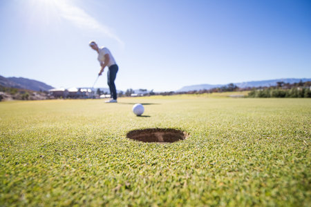 Close up wide angle view of a golfer about to put a ball into the hole on a green on a golf course in South Africaの写真素材