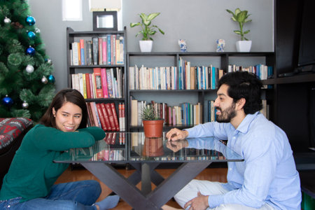 Couple flirting in the living room with a bookshelf and a christmas tree in the background