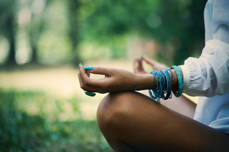 woman meditate  in wood, close up of legs, hands and part of body in white shirt, selective focus on hand, side viewの写真素材
