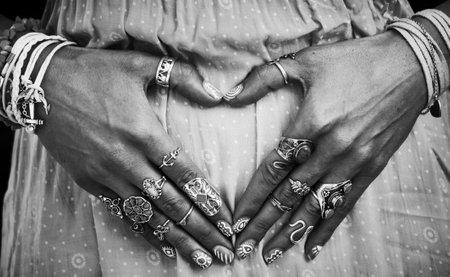 closeup of young woman hands in heart shape with lot of boho style jewrly, rings and bracelets outdoor summer day close up black and whiteの写真素材