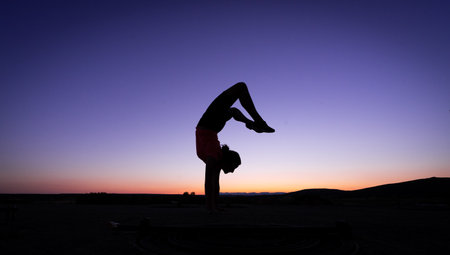 silhouette of a teenage girl exercising, jumping and gymnastics at sunset last night. purple and orange sky in the background.の写真素材