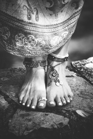 woman summer boho fashion style barefoot with jewelry anklets and rings stand on stone outdoor summer day bwの写真素材
