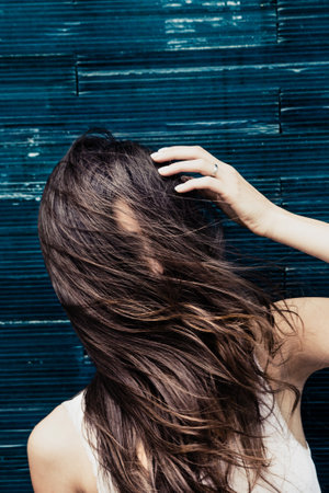 young woman lean on tiled wall wind in hairの写真素材