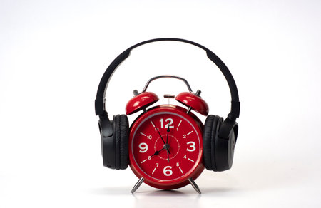 Red Alarm Clock put on headphones over white background, Timeless Music Concept. Copy spaceの写真素材