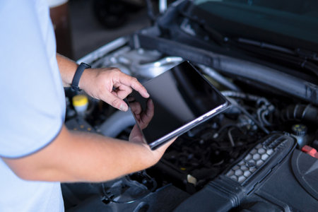 Auto mechanic with digital tablet at work making an engine repair diagnosis of a car in a mechanic garageの写真素材
