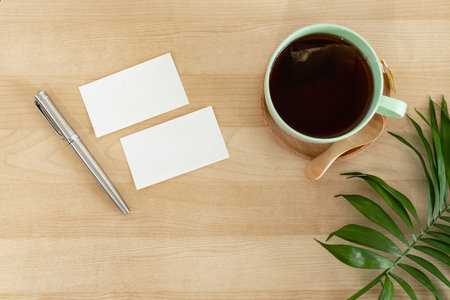 Business card, green leaves and tea cup on wooden desk.の写真素材