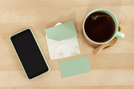 Recycled paper card, envelope, tea cup, pen with smart phone, on a wooden table.の写真素材