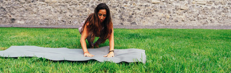 Young yogi placing his mat on the grass in the park to start doing yoga