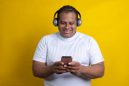Hispanic man listening to music with headphones and cell phone, on yellow backgroundの写真素材