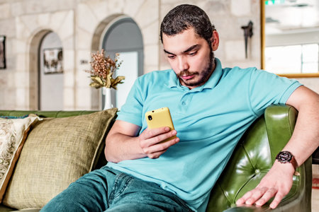 Serious man watching media content in a smart phone sitting on a couch at home.