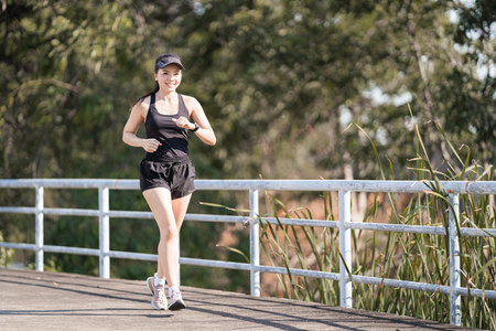 A healthy happy Asian woman runner in black sport outfits jogging in the natural city park under evening sunsetの写真素材