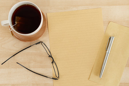 Blank letter paper and envelope, tea cup, on wooden office desk.の写真素材