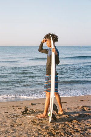 Profile of afro surfer with surfboards looking to the horizon on the beach at sunrise.