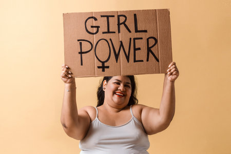 Latinx adult woman holding up hands with "girl power" banner over.の写真素材