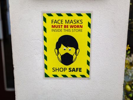 A wall sign stating that face masks must be worn while inside the store. Comedy googly eyes have been stuck on the eyesの写真素材