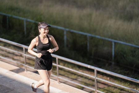 A healthy happy Asian woman runner in black sport outfits jogging in the natural city park under evening sunsetの写真素材