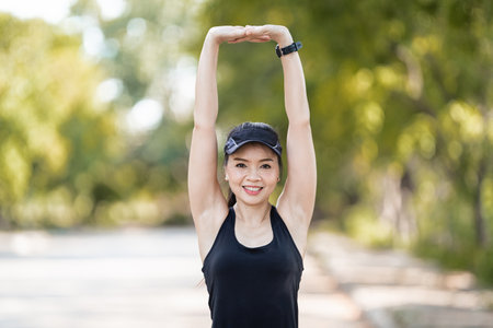 A cheerful Asian female runner in sports outfits doing stretching before jogging exercise outdoor in the city natural park under evening sunsetの写真素材