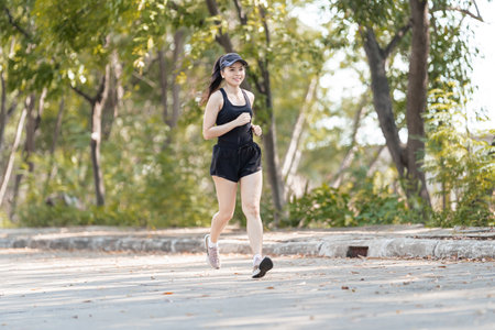 A healthy happy Asian woman runner in black sport outfits jogging in the natural city park under...