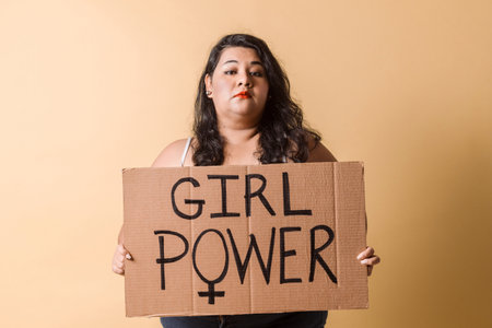 Adult latinx woman hold a placard. feminism concept. Oversized woman looking away and smiling with "girl power"banner over.の写真素材