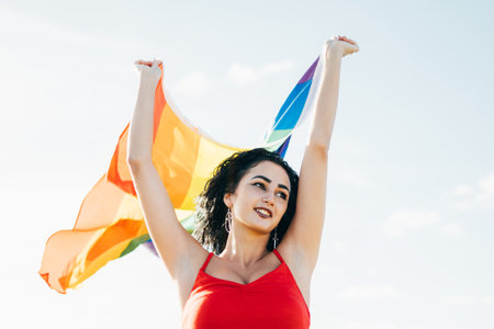 Transsexual female carries a gay pride lgbt flag that moves on a sunny day with the breeze.She is struggling for sexual liberty.の写真素材