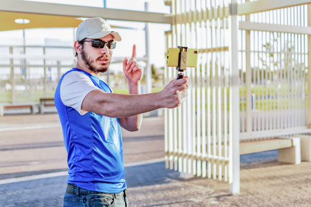 Young man blogger talking with followers, live streaming in social media, looking to smart phone screen.の写真素材
