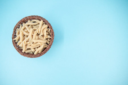 shot of italian torchiette pasta in a wicker canister on a cyan color backgroundの写真素材