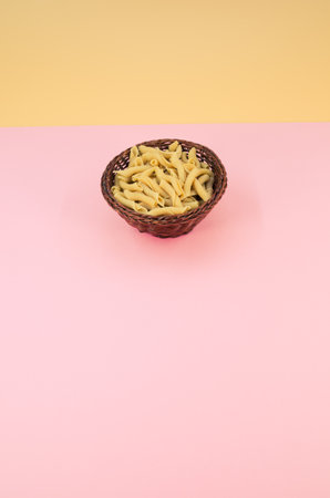 shot of italian torchiette pasta in a wicker canister on a pink color backgroundの写真素材