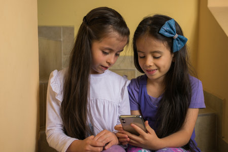 two latin girls sitting on the stairs see the cell phone