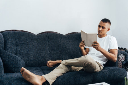 Young hispanic man reading a book. Man study sit on sofa.の写真素材