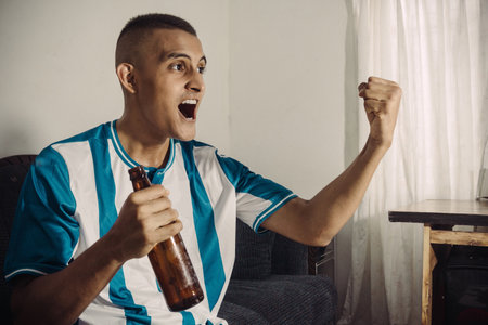 Excited Hispanic Man watching tv sitting on a sofa in the living room at home.の写真素材