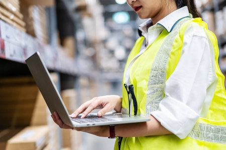 Asian engineer woman check stock details on tablet computer for checking boxes with logistics on shelves with goods background in warehouse, logistic and business exportの写真素材