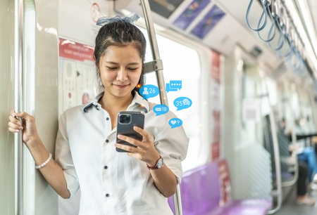 Young Asian woman passenger standing and using cell phone inside empty subway or sky train car, leisure and daily lifeの写真素材