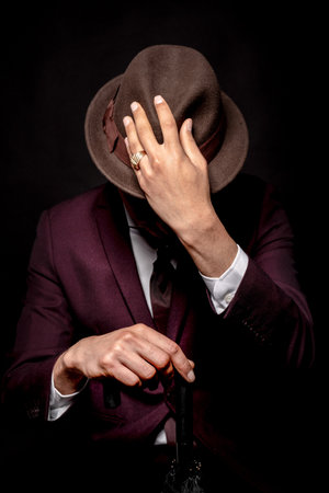 Man in suit hiding face behind his hat isolated on dark background. secret and incognito conceptの写真素材