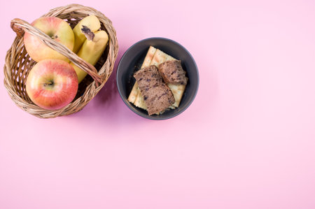A closeup of tasty crackers with bread and fruits in a basket and bowl on pink backgroundの写真素材