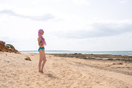 Woman with pink scarf for cancer looking at the sea in bikini from the beachの写真素材