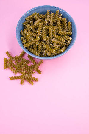 Vertical shot of  italian fusilli pasta in a blue bowl on a pink background with text spaceの写真素材