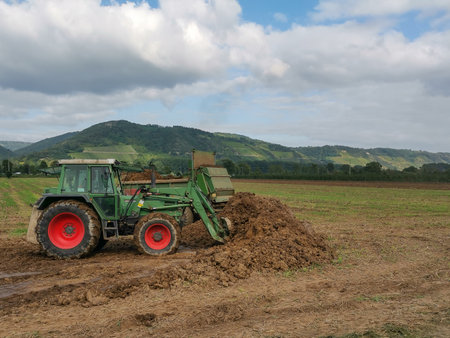 A tractor on a wide field loading earth onto a trailer
